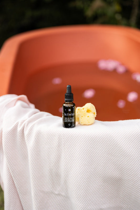 Sun to Moon Serum op de rand van een bad met bloemblaadjes in de tuin