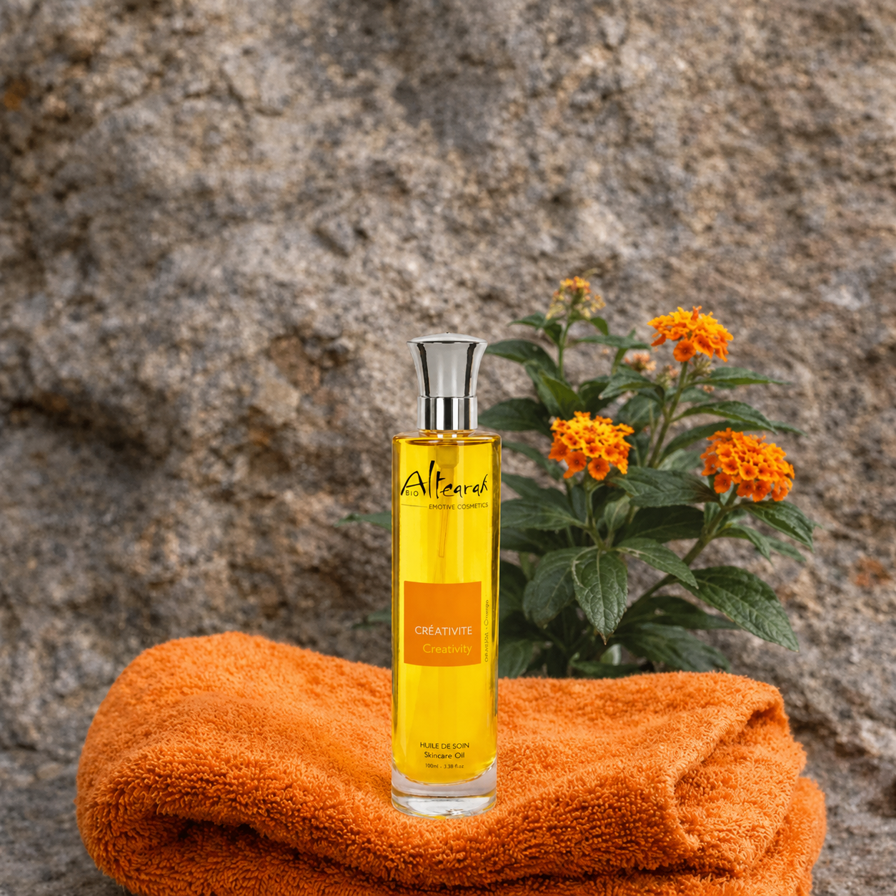 Altearah Orange Creativity olie op handdoek met bloemen en rots ontspannend wellness moment energie en balans